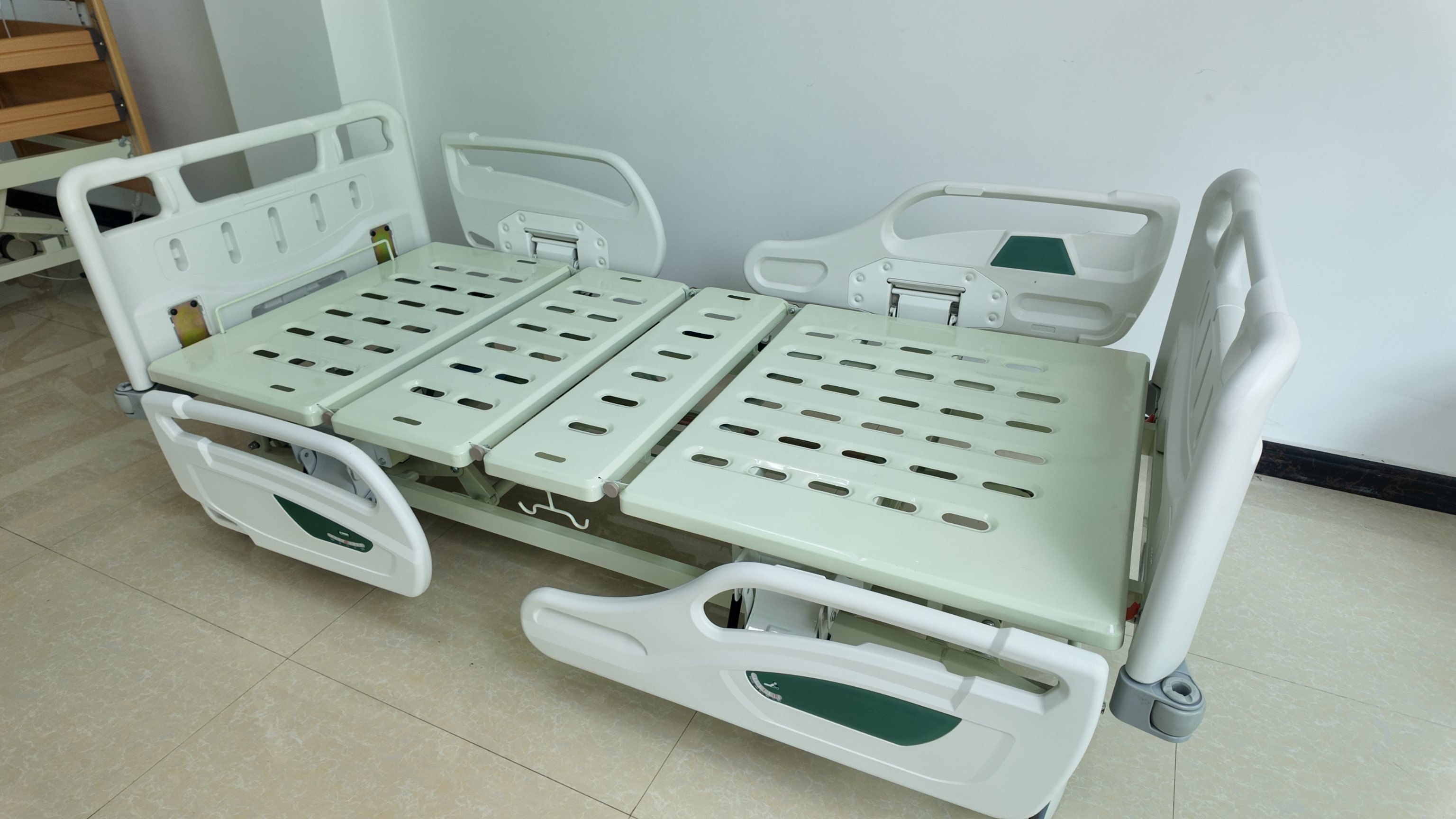Side view of the three-function manual hospital bed with green headrest